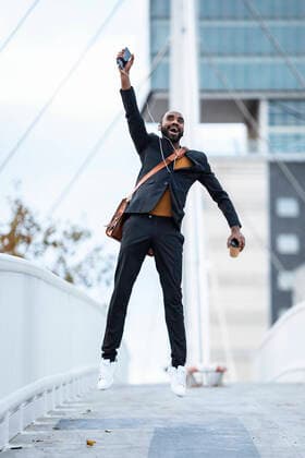 Happy young businessman with coffee to go, smartphone and earphones jumping in the air model released Symbolfoto  JSRF00715