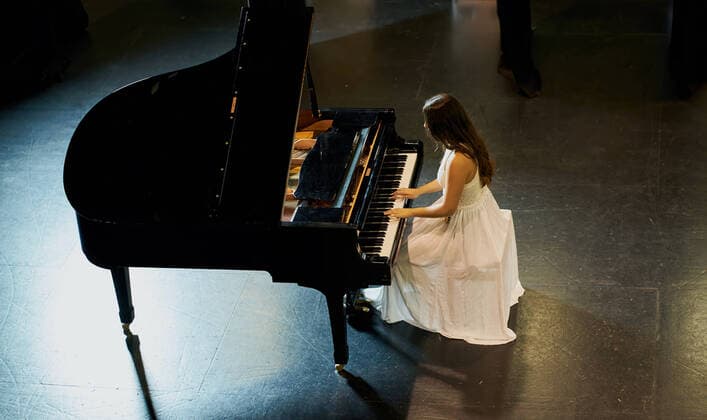 A woman with brown hair dressed in a white dress seen playing a black grand piano with the lid raised. View from above of the pianist Berriozar, Navarre, Spain CR_SEBO200105D-267910-01