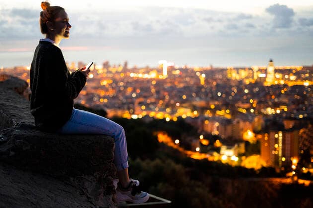 Young woman sitting on railing above the city using cell phone, Barcelona, Spain model released Symbolfoto  GIOF07941