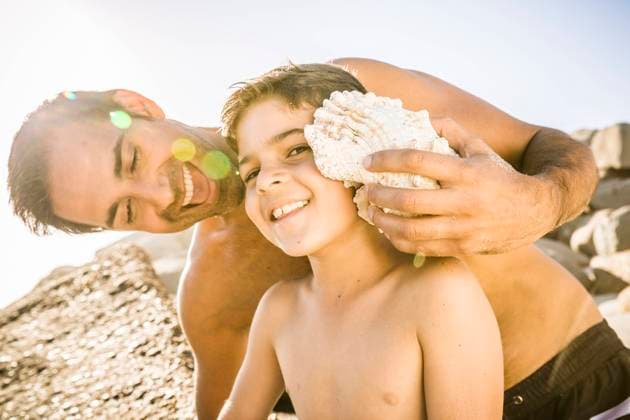 Father and son having fun on the beach and listening to the ocean in a shell model released Symbolfoto  SDAHF00486