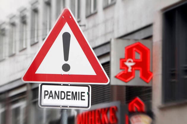 Photomontage symbolic image of the spread of the coronavirus and the public handling of the disease Traffic sign Attention Danger with addition Pandemic in front of the logo of a pharmacy in Frankfurt, Hesse, Germany