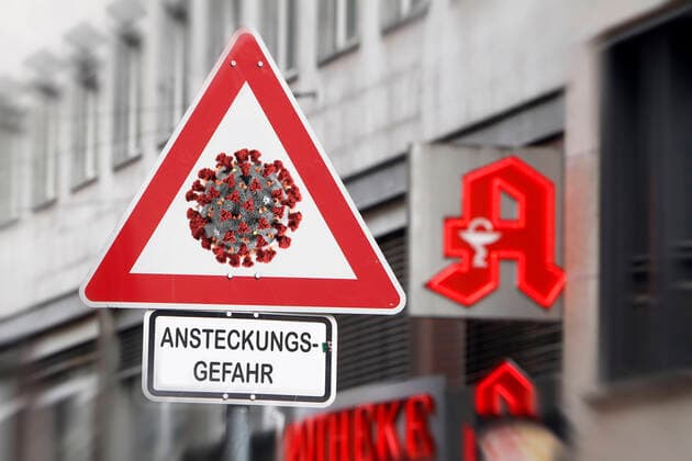 Photomontage symbolic image of the spread of the coronavirus and the public handling of the disease Traffic sign Attention Coronavirus with additional risk of infection in front of the logo of a pharmacy in Frankfurt, Hessen, Germany