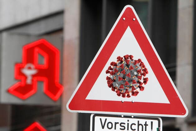 Photomontage symbolic image of the spread of the coronavirus and the public handling of the disease Traffic sign Attention Coronavirus with the addition of Caution before the logo of a pharmacy in Frankfurt, Hesse, Germany