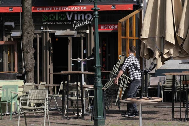 A man puts away chairs outside closed bars, cafes and restaurants as a sign reads Do Like the Italians Do outside an Italian restaurant March 16, 2020 in The Hague, Netherlands.  (124471043)