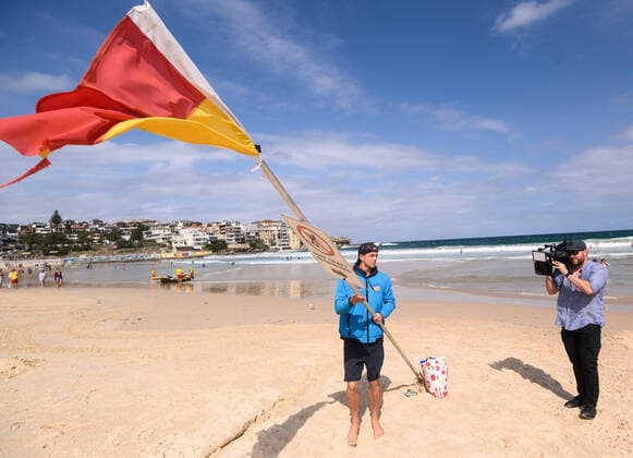 BONDI BEACH CORONAVIRUS CLOSURE, A surf life saver brings down a red and yellow flag as Bondi Beach was closed this afternoon in Sydney, Saturday, March 21, 2020. Beachgoers drew condemnation yesterday when tens of thousands of people flouted social distancing rules, which have been put in place in an effort to limit the spread of COVID-19. ( NO ARCHIVING, EDITORIAL USE ONLY, NO USE IN BOOKS WITHOUT CONSENT SYDNEY NSW AUSTRALIA  Copyright: xJAMESxGOURLEYx 20200321001458559136