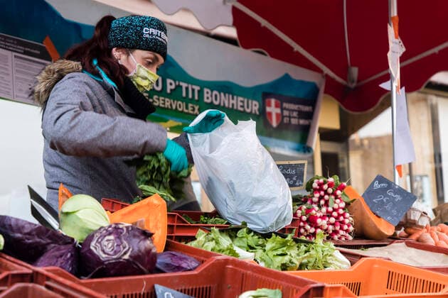 Chambery, France March 21, 2020 - Morning atmosphere at the downtown market during the period of confinement due to the coronavirus health crisis - A saleswoman wearing a sanitary mask serves vegetables to customers EPIDEMIE, CORONAVIRUS, VIRUS, CRISE SANITAIRE, COVID19, VIE QUOTIDIENNE, MARCHE, ALIMENTAIRE, COMMERCANTS, RESTRICTIONS, PANDEMIE, SANTE, AMBIANCE, ATMOSPHERE, CONFINEMENT, INQUIETUDES, FAIRE DES COURSES, RESTRICTIONS DE CIRCULATION, APPROVISIONNEMENT, PRODUITS DE PREMIERE NECESSITE, MALADIE, CHAMBERY, SAVOIE, PROPAGATION DU VIRUS, ALIMENTATION, MASQUE SANITAIRE, LEGUMES Copyright: xVincentxIsorex