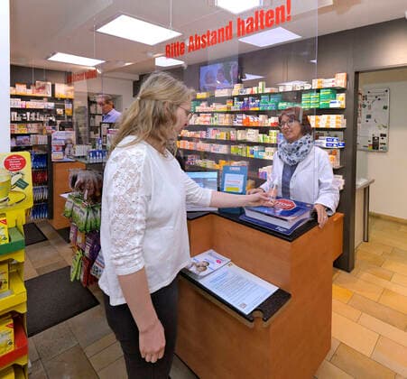 21 03 2020, protective glass at the cash desk of a pharmacy in Pfaffenhausen in Lower Allgäu due to corona virus pandemic A plexiglass pane was hung up between the pharmacy specialist and the customers, with the inscription Please keep your distance li Owner Katharina Großmann of St Josefs Pharmacy presents a customer situation with pharmacy special
