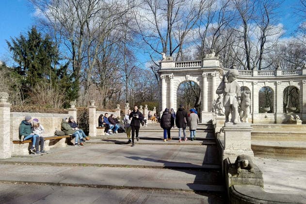 21 03 2020, Berlin Germany People enjoy a place in the sun in bright weather and sit on benches at the fairy tale fountain despite the corona crisis