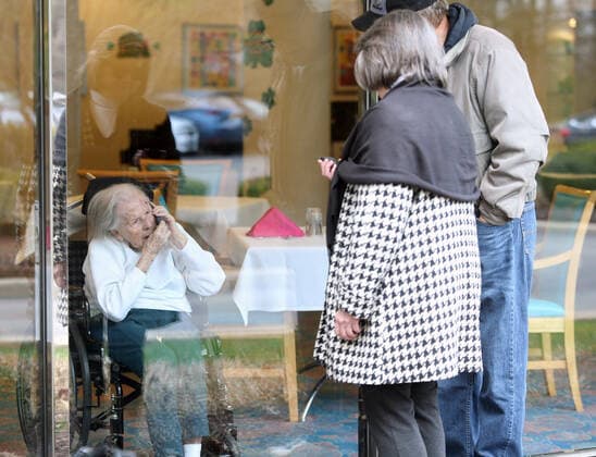 Wilma Grove uses a cell phone to talk to her children, Judy Kekich and Ed Grove during their visit to Delmar Gardens on the Green in Ballwin, Missouri on March 21, 2020. The family has been forced to visit their 100 year-old mother every day from the outside due to Coronavirus concerns. Missouri s known cases of COVID-19, is at 73 including three deaths.  SLP2020032102 BILLxGREENBLATT