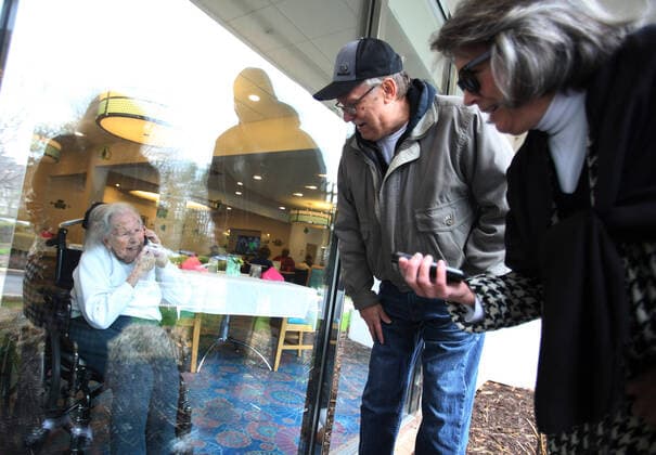 Wilma Grove uses a cell phone to talk to her children, Judy Kekich and Ed Grove during their visit to Delmar Gardens on the Green in Ballwin, Missouri on March 21, 2020. The family has been forced to visit their 100 year-old mother every day from the outside due to Coronavirus concerns. Missouri s known cases of COVID-19, is at 73 including three deaths.  SLP2020032104 BILLxGREENBLATT