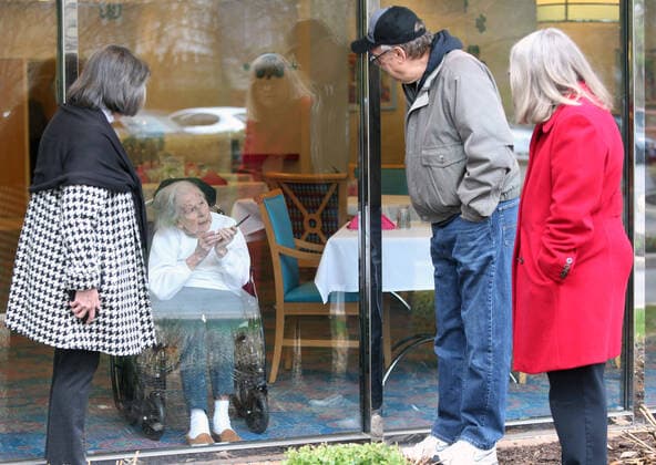 Wilma Grove uses a cell phone to talk to her children (L to R) Judy Kekich, Ed Grove and Pat Grove during a visit at Delmar Gardens on the Green in Ballwin, Missouri on March 21, 2020. The family has been forced to visit their 100 year-old mother every day from the outside due to Coronavirus concerns. Missouri s known cases of COVID-19, is at 73 including three deaths.  SLP2020032105 BILLxGREENBLATT
