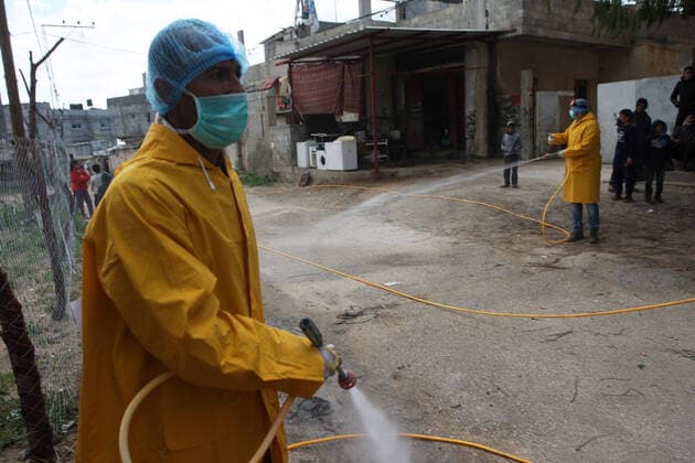 Palestinian volunteers wearing protective clothes and masks disinfect a street as a preventive measure against the spread of novel coronavirus, in Rafah in the southern Gaza Strip, on Sunday, March 22, 2020. Authorities in Gaza today confirmed the first two cases of novel coronavirus, identifying them as Palestinians who had traveled to Pakistan and were being held in quarantine since their return. The United Nations has warned that a COVID-19 outbreak in Gaza could be disastrous, given the high poverty rates and weak health system in the coastal strip under Israeli blockade since 2007.  GAZ2020032209 ISMAELxMOHAMAD