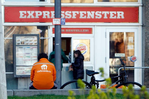 Bicycle courier from the Internet portal Lieferando waits in front of an express window of a Burger King store for an order to be delivered to a customer in downtown Mannheim, Hesse, Germany