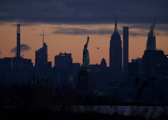 The sun rises on the Empire State Building, the Statue of Liberty and the Manhattan in New York City on Tuesday, March 24, 2020. New York City Mayor Bill de Blasio said the number of positive cases in the city was at 13,119 as of 6 p.m. on Monday.  NYP20200324105 JOHNxANGELILLO