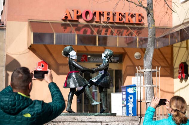 Unknown persons have attached breathing masks to the statue of two dancing girls in the centre of Jena The statue is standing in front of a pharmacy Two passers-by take a picture of the statue Photo of 24 3 2020