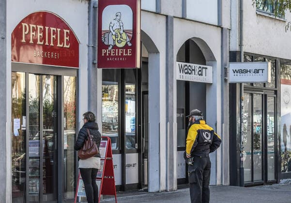 A postman stands at a safe distance in front of an open bakery in an otherwise almost deserted city Public life is largely shut down, shops and stores closed, mail, garbage collection and other system-relevant professions are still on the move in Freiburg Photo Winfried Rothermel