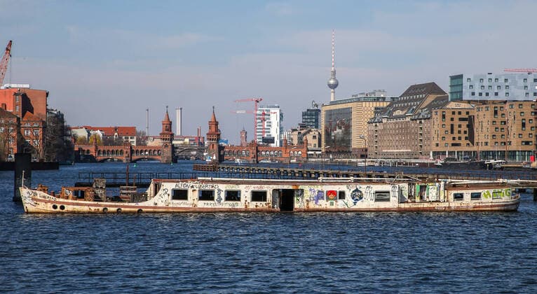 Ship Dr Ingrid Wengler Berlin, 25 03 20, view over the river Spree to Oberbaumbruecke and skyline with television tower In front deserted wreck ship Dr Ingrid Wengler Berlin Berlin Germany Spree river bank