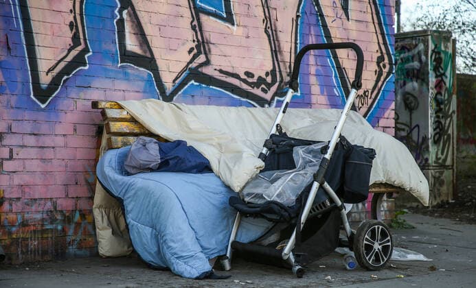 Coronavirus in Berlin Berlin, 25 03 2020, Kreuzberg A homeless man sleeps under blankets at almost 3 degrees outside temperature on a park bench under a bridge A pram for the transport of his belongings stands next to him During the coronavirus crisis homeless people have to fight as risk groups with massive restrictions of their basic care and medical assistance Berlin Berlin Germany Kreuzberg
