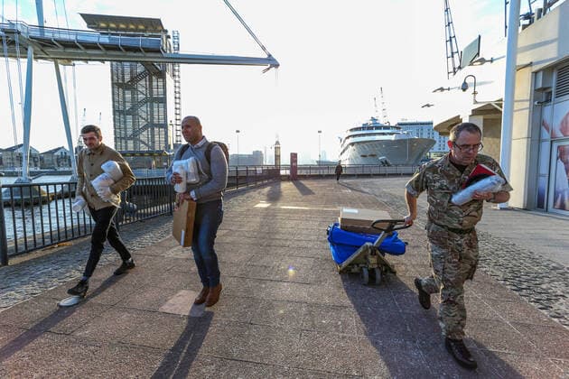 A British Army soldier accompanied by two civilians pulling a cart with medical supplies is seen outside the ExCell Center in London, Thursday, March 26, 2020. The British Government announced Tuesday, that the ExCel Center in east London will become a 4,000 bed temporary hospital to deal with future coronavirus patients, to be called NHS Nightingale. The new coronavirus causes mild or moderate symptoms for most people, but for some, especially older adults and people with existing health problems, it can cause more severe illness or death 