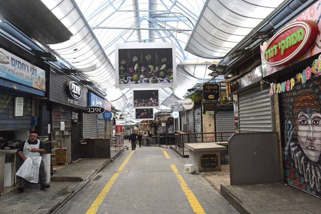 An Israeli vendor sits outside his half-shuttered shop in the partically closed Mahane Yehuda Market in Jerusalem, on Friday, March 27, 2020. Eleven Israelis have died from the coronavirus, while more than 3,000 have been diagnosed with the disease. The Israeli government has imposed tight restrictions of movement, leaving only essential stores open in an effort to stop the spread of the coronavirus.  JER2020032705 DEBBIExHILL