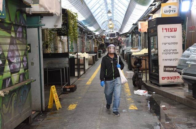 A man wears a protective face shield and gloves in the partically closed Mahane Yehuda Market in Jerusalem, on Friday, March 27, 2020. Eleven Israelis have died from the coronavirus, while more than 3,000 have been diagnosed with the disease. The Israeli government has imposed tight restrictions of movement, leaving only essential stores open in an effort to stop the spread of the coronavirus.  JER2020032709 DEBBIExHILL