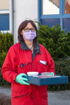 Woman with mouthguard delivers food from to household, food on wheels Impressions from the time of the curfew in the Coronavirus Pandemic in Bavaria Impressions Outside in the curfew Corona Virus