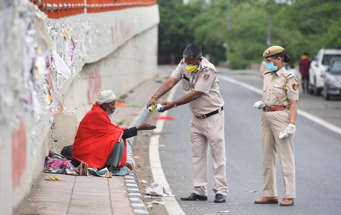 NEW DELHI, INDIA - MARCH 27: Delhi Police personnel offers hand sanitizer to a homeless man on the third day of the national lockdown imposed by Prime Minister Narendra Modi to curb the spread of Coronavirus COVID-19 near Akshardham temple foot over Bridge, on March 27, 2020 in New Delhi, India. They also distributed food to the workers and the homeless on the road. (Photo by Raj K Raj Hindustan Times) Government Provide Food To Homeless And Poor Amid Lockdown To Prevent Covid 19