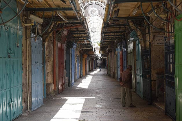 Palestinians walk past shuttered shops, on an empty street, in Jerusalem s Old City, in compliance with coronavirus movement restrictions, on Saturday, March 28, 2020. The Israeli government has imposed tight restrictions of movement, leaving only essential stores open in an effort to stop the spread of the coronavirus disease.  JER2020032814 DEBBIExHILL