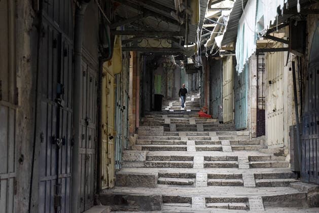 A Palestinian walks past shuttered shops, on an empty street, in Jerusalem s Old City, in compliance with coronavirus movement restrictions, on Saturday, March 28, 2020. The Israeli government has imposed tight restrictions of movement, leaving only essential stores open in an effort to stop the spread of the coronavirus disease.  JER2020032817 DEBBIExHILL