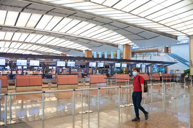 28 03 2020, Singapore, Republic of Singapore, Asia A man walks past closed check-in counters in the empty departure hall of Terminal 2 at Changi Airport, wearing a respirator to protect himself from infection with the pandemic corona virus The global spread of the virus has drastically reduced the number of flights worldwide, resulting in significant flight cancellations