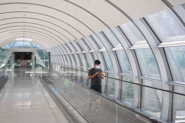 28 03 2020, Singapore, Republic of Singapore, Asia A man walks along the bridge connecting Jewel Terminal and Terminal 2 at Changi Airport, wearing a respirator to protect himself from infection with the pandemic corona virus
