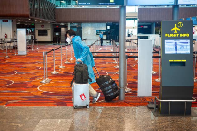 28 03 2020, Singapore, Republic of Singapore, Asia A passenger arrives with his or her baggage at a check-in counter in Terminal 1 at Changi Airport and wears a respirator and raincoat to protect against infection with the pandemic corona virus The flight with China Southern Airlines to Guangzhou Canton is one of only a few that are still taking place after massive