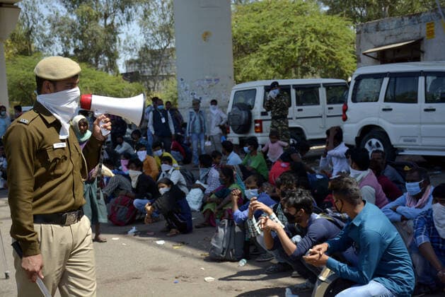 GHAZIABAD, INDIA - MARCH 29: A police personnel keeps watch at migrant workers as they prepare to head to their native state on Day 5 of the 21 day nationwide lockdown imposed by PM Narendra Modi to curb the spread of coronavirus, at Anand Vihar Bus Terminus, on March 29, 2020 in Ghaziabad, India. (Photo by Sakib Ali Hindustan Times ) Migrant Workers Head Home In Coronavirus Lockdown