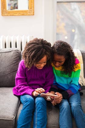 Sisters looking at smart phone while sitting on sofa in living room New York, NY, United States ,model released, Symbolfoto ,property released CR_LIWEEE200227-318356-01