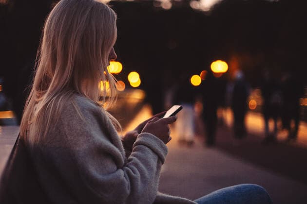 Young woman using smart phone while sitting on bench in city at dusk ,model released, Symbolfoto CR_DMBE200313-307694-01