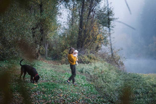 A woman is holding a baby and looking at a dog near a river United States, California, Monte Rio ,model released, Symbolfoto CR_EVVA200323E-301734-01