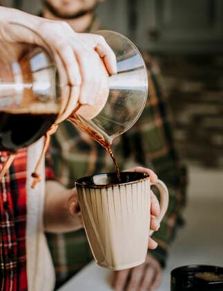 hot coffee is poured from a pour over into a tan coffee cup Poland, ME, United States ,model released, Symbolfoto CR_SSNF200327-319274-01