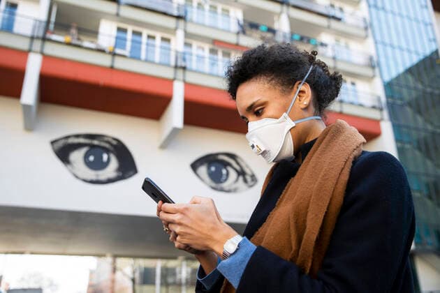 Eine Junge Frau schaut aud ihr Handy mit den Augen eines Grafitti im Hintergrund am 1. April 2020. Um die Verbreitung des Coronavirus (SARS-CoV-2) zu verlangsamen beschlossen Bund und Laender weitere Restriktionen. Nachdem Museen, Theatern, Sportveranstaltungen usw verboten wurden sind seit einigen Tagen weitere verschaerfte Massnahmen in Kraft getreten wie z.B. Verbot von Versammlungen in der Oeffentlichkeit mit mehr als zwei Personen, Einhaltung von Mindestabstand zwischen Personen und Schliessung von Gastronomiebetrieben mit Ausnahme von Abholung und Lieferung. Es wird diskutiert ob die Nutzung und Auswertung oder gar die Kontrolle der Handydaten zur Eindaemmung der Verbreitung der Virus mit der Verfassung und den Respekt der Grundrechte sei. Achtung: Illustrative Editorial. MR = Yes Diskussion ueber moegliche Kontrolle von Handydaten
