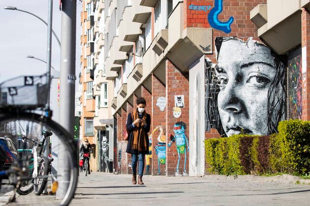 Eine Junge Frau schaut aud ihr Handy mit den Augen eines Grafitti im Hintergrund am 1. April 2020. Um die Verbreitung des Coronavirus (SARS-CoV-2) zu verlangsamen beschlossen Bund und Laender weitere Restriktionen. Nachdem Museen, Theatern, Sportveranstaltungen usw verboten wurden sind seit einigen Tagen weitere verschaerfte Massnahmen in Kraft getreten wie z.B. Verbot von Versammlungen in der Oeffentlichkeit mit mehr als zwei Personen, Einhaltung von Mindestabstand zwischen Personen und Schliessung von Gastronomiebetrieben mit Ausnahme von Abholung und Lieferung. Es wird diskutiert ob die Nutzung und Auswertung oder gar die Kontrolle der Handydaten zur Eindaemmung der Verbreitung der Virus mit der Verfassung und den Respekt der Grundrechte sei. Achtung: Illustrative Editorial. MR = Yes Diskussion ueber moegliche Kontrolle von Handydaten