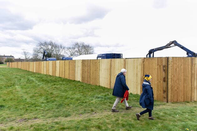 . 02 04 2020. London, United Kingdom. Coronavirus crisis. Passers by seen walking next to the fence where the new mortuary is being building. A new mortuary for coronavirus victims, is been building on forest land next to the City of London Cemetery and Crematorium and is expected to take the dead from the new Nightingale Hospital at the ExCel Centre.  xGustavoxValientex xi-Imagesx IIM-20974-0013