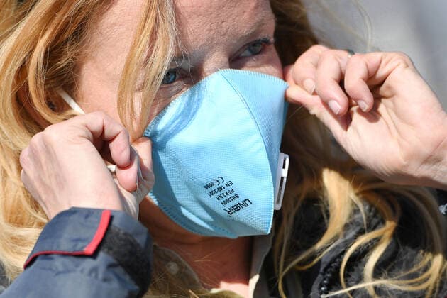 A woman puts on an FFP2 mask in her face Mask,protective mask,mouthguard Virus protection, too many corona infections Munich Helios Clinic is closing down Because of a large number of corona infections among patients and staff, the Munich clinic is temporarily closing down normal hospital operations The emergency department is also affected The chains of infection are to be broken, on 02 04 2020