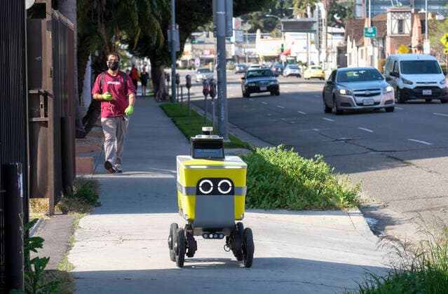 April 2, 2020, Los Angeles, California, U.S: A man wearing a face mask walks behind a food delivery robot as it make its way on April 2, 2020 in Los Angeles. Los Angeles Mayor Eric Garcetti is advising the public to wear any kind of protective face covering when going out -- even a scarf or other clothing item -- to reduce the spread of the coronavirus. Los Angeles U.S. - ZUMAc68_ 20200402_zaf_c68_008 Copyright: xRingoxChiux