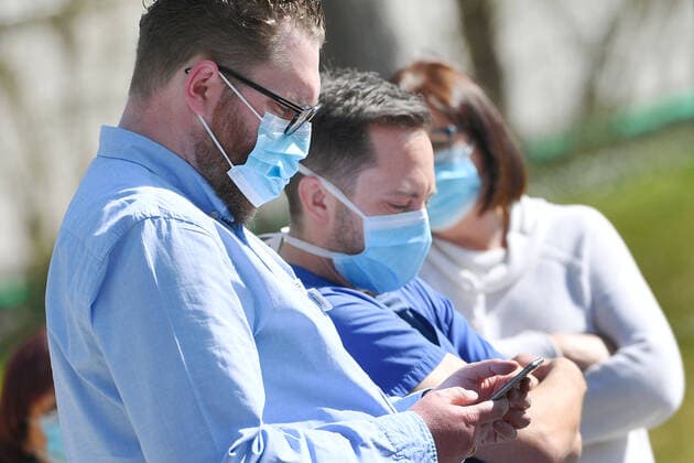 Persons wearing face masks,face masks,masks,face masks Nose protection,mouth nose protection A man looks at his smartphone,tracking app,tracing app Handyapp Too many corona infections Munich Helios Clinic is closing down Because of a large number of corona infections among patients and staff, the Munich clinic is temporarily closing down normal ho