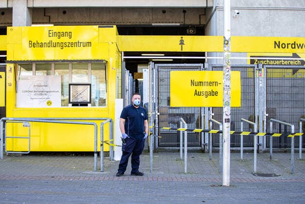 (200405) -- DORTMUND, April 5, 2020 (Xinhua) -- A security member wearing a protective mask stands guard outside the COVID-19 testing center at Borussia Dortmund s stadium in Dortmund, Germany, April 4, 2020. Borussia Dortmund s stadium housed a COVID-19 testing center From Saturday. Rooms in the Westfalenstadion s north stand have been prepared to take in people suspected of suffering from COVID-19. It is hoped the center will relieve pressure on the medical facilities in the city of Dortmund. (Photo by Joachim Bywaletz Xinhua) (SP)GERMANY-DORTMUND-STADIUM-COVID-19-TESTING CENTER 