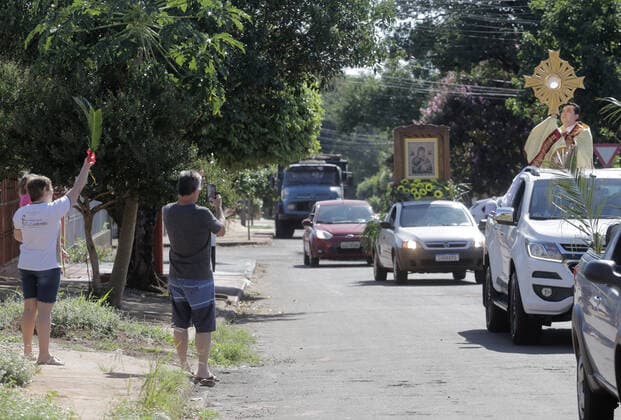 Coronavirus in Brasilien, motorisierte Prozession zum Beginn der Karwoche in Campo Mourao CAMPO MOURÃO, PR - 05.04.2020: COVID 19 ESPANTA FIES NO DOMINGO DE RAMOS - Catholics in Campo Mourão, in the Midwest Region of Paraná, celebrated Palm Sunday? beginning of Holy Week? from the gate into the residences. The faithful placed a green branch on the gates of the houses waiting for the passage of the Most Holy. Due to the recommendation of social isolation due to the Covid-19 pandemic, a disease caused by the coronavirus, a priest held a small procession blessing the homes and people of neighborhoods close to the city center. In the photo, faithful celebrate Palm Sunday from the gate of their homes. x1901695x  DirceuxPortugal