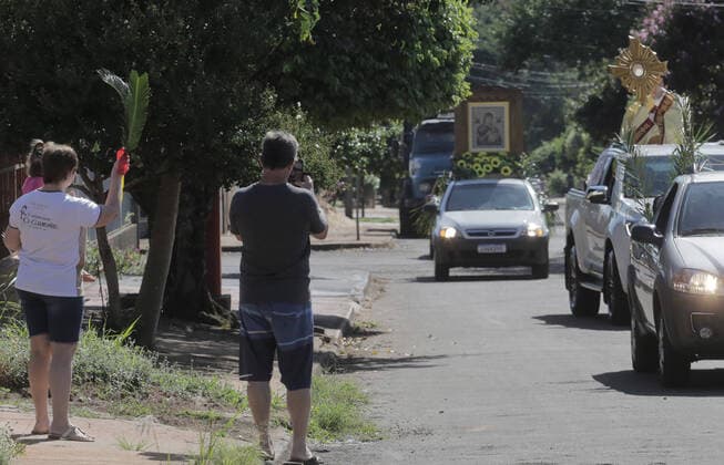 Coronavirus in Brasilien, motorisierte Prozession zum Beginn der Karwoche in Campo Mourao CAMPO MOURÃO, PR - 05.04.2020: COVID 19 ESPANTA FIES NO DOMINGO DE RAMOS - Catholics in Campo Mourão, in the Midwest Region of Paraná, celebrated Palm Sunday? beginning of Holy Week? from the gate into the residences. The faithful placed a green branch on the gates of the houses waiting for the passage of the Most Holy. Due to the recommendation of social isolation due to the Covid-19 pandemic, a disease caused by the coronavirus, a priest held a small procession blessing the homes and people of neighborhoods close to the city center. In the photo, faithful celebrate Palm Sunday from the gate of their homes. x1901703x  DirceuxPortugal