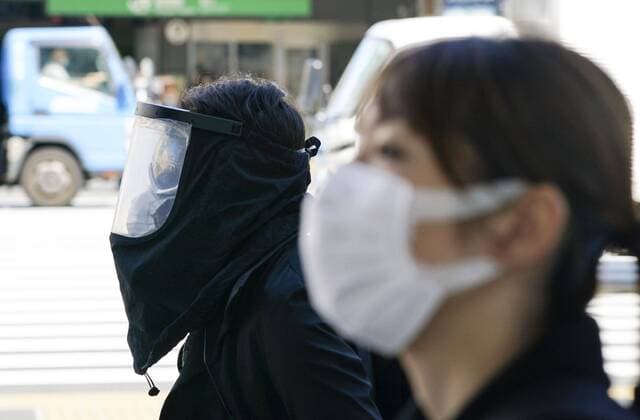 Coronavirus in Japan, Eindrücke aus Tokio New coronavirus A man (L) walks with his face fully covered with a protective shield in front of JR Shinjuku Station in Tokyo on April 6, 2020, amid the spread of the coronavirus. 