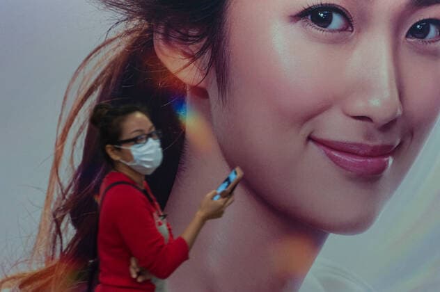 02 04 2020, Singapore, Republic of Singapore, Asia A woman walks past an advertising space in a pedestrian underpass, wearing a respirator to protect herself from infection with the pandemic corona virus