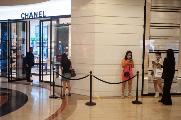 02 04 2020, Singapore, Republic of Singapore, Asia Women queuing in front of a shop of the luxury brand Chanel in the Takashimaya shopping mall wearing a respirator to protect themselves from infection with the pandemic corona virus