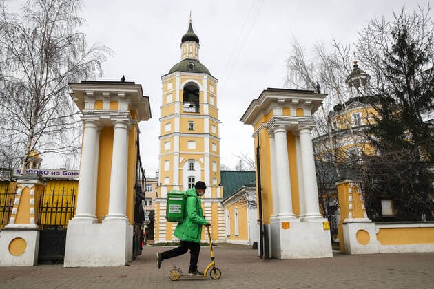 MOSCOW, RUSSIA - APRIL 6, 2020: A courier of the Delivery Club food delivery service riding a kick scooter by the Church of Philip II, Metropolitan of Moscow amid the ongoing COVID-19 coronavirus pandemic. The Moscow authorities imposed home isolation for all residents, regardless of their age, and restrictions on movement within the city, effective since March 30, 2020; a period off work with full pay was extended until April 30 nationwide as part of preventive measures to contain the spread of the COVID-19 infection. Artyom Geodakyan TASS  TS0D49D4